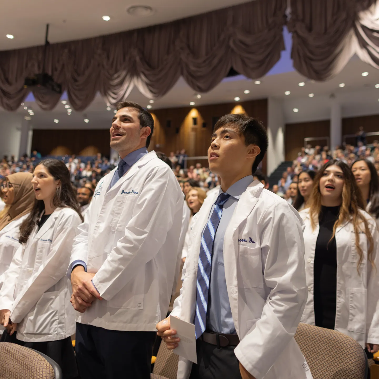 Students don their white coats and rise to recite an oath of professionalism in Robbins Auditorium.