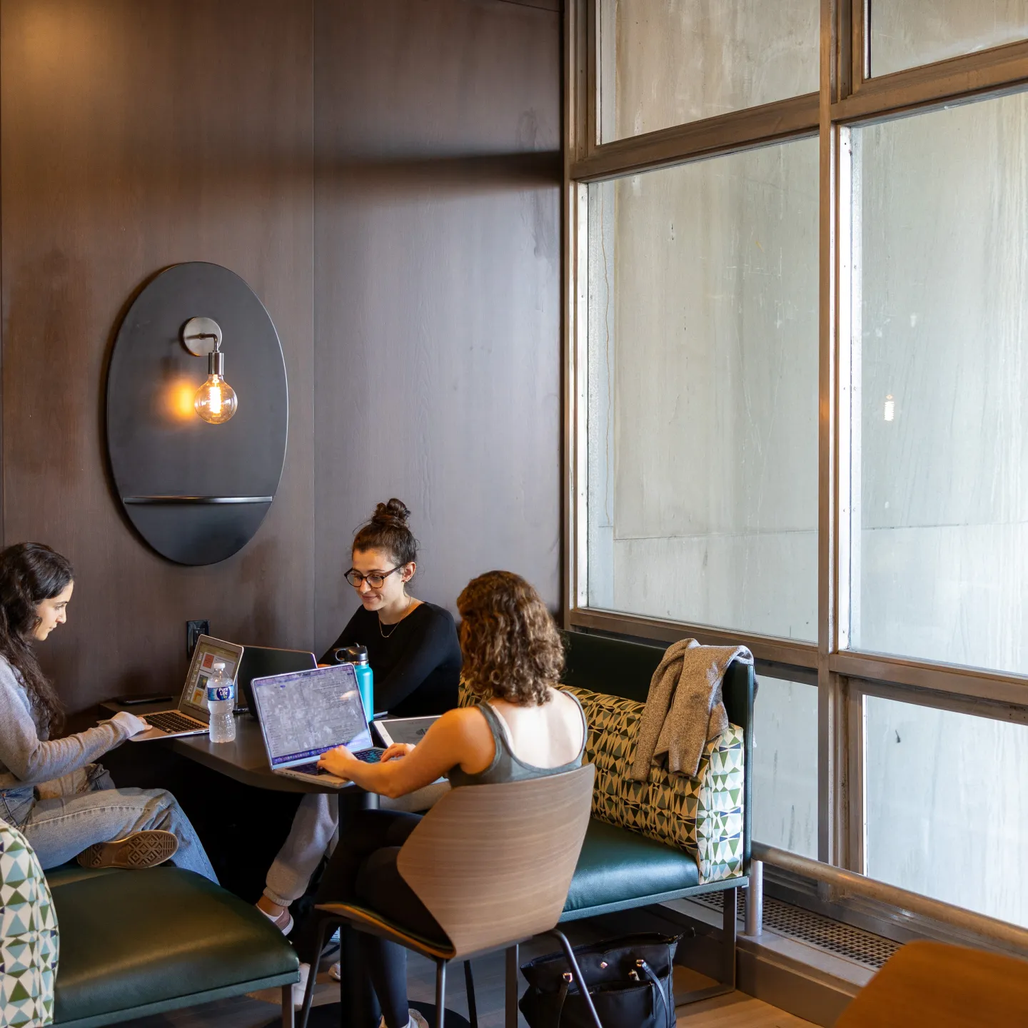 Three students, seated in a semicircle and working on computers, share a booth in the upper level of Albert’s Den. 