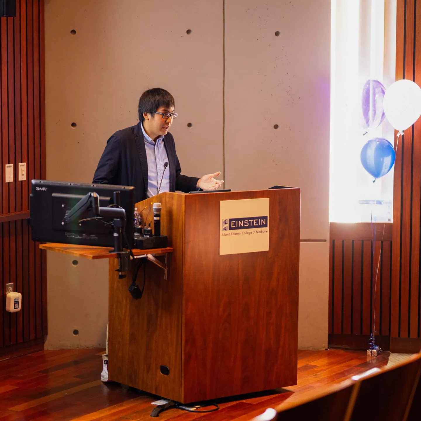 Junichi Okada presenting at podium in Lefrak Auditorium