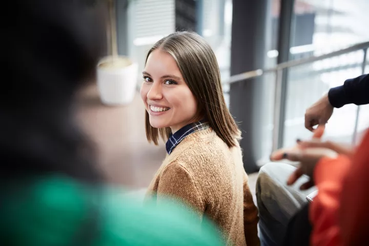 A student in a brown cardigan looks back at another student while walking through campus