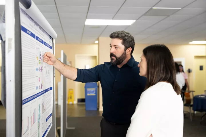 Two people discuss research in front of a poster during Einstein’s annual Research Day. 