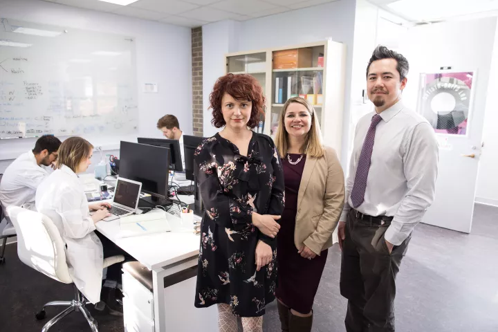 Research mentors Dr. Renata Batista Brita, Dr. Luke Sjulson, and Dr. Anita Autry-Dixon (left to right) next to a group of scientists working on computers