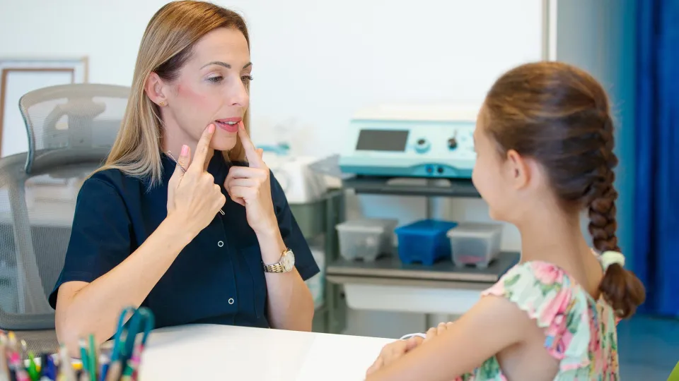 Female speech therapist showing mouth articulation, guiding girl in session